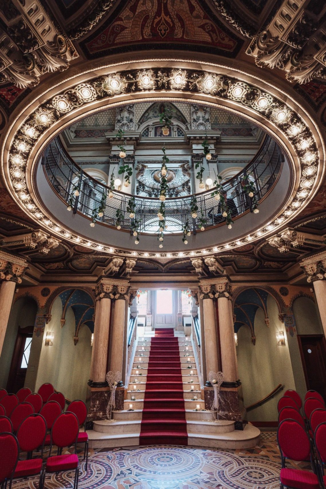 Prächtige Treppe mit rotem Teppich, Kronleuchter und eleganter Architektur im Foyer.