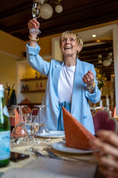 Eine fröhliche Frau hebt ein Glas in einem eleganten Restaurant.