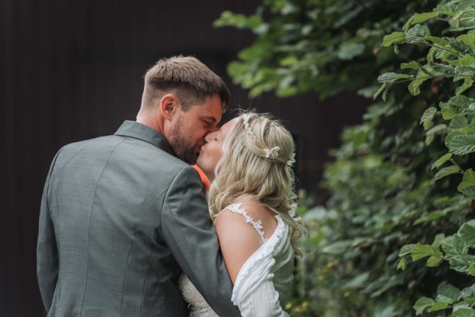Ein Brautpaar küsst sich romantisch vor einer grünen Hintergrundlandschaft.
