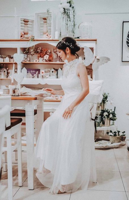 Braut in einem eleganten, weißen Kleid sitzt an einem Tisch und betrachtet etwas.