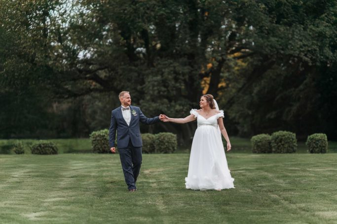 Ein Paar in festlicher Kleidung spaziert Hand in Hand über eine Rasenfläche.