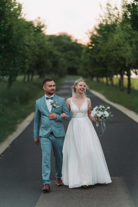 Braut und Bräutigam in festlicher Kleidung gehen glücklich einen Weg entlang.