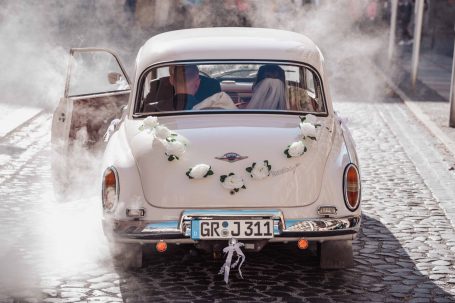 Hochzeitsauto mit Blumen geschmückt, Vintage-Stil, auf einer Kopfsteinpflasterstraße.