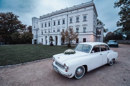 Ein klassisches weißes Auto vor einem eleganten, historischen Gebäude.