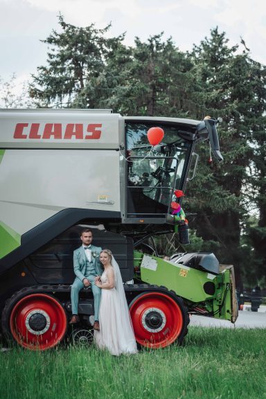 Brautpaar posiert vor einem großen CLAAS Mähdrescher im Freien.