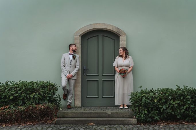 Ein Paar steht vor einer grünen Tür, umgeben von grüner Bepflanzung.