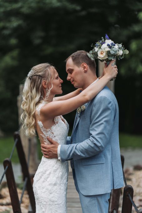 Braut und Bräutigam umarmen sich leidenschaftlich auf einer Brücke im Freien.