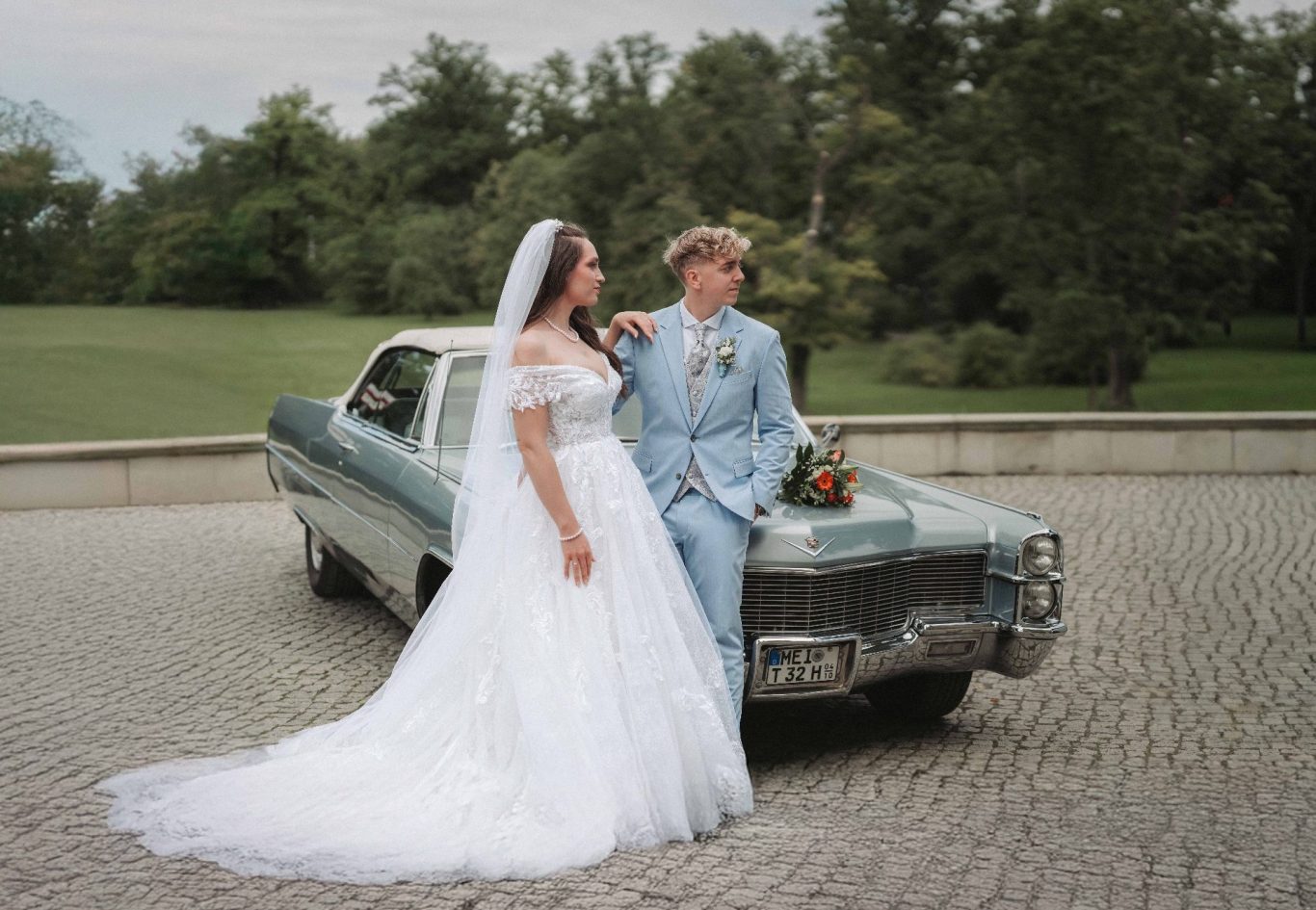 Braut mit offenem Rücken und Spitzenärmel, Brautpaar umarmt sich von hinten.