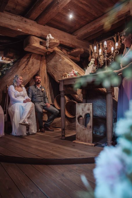 Hochzeitszeremonie in rustikalem Raum mit Kerzen und Brautpaar an einem Tisch.