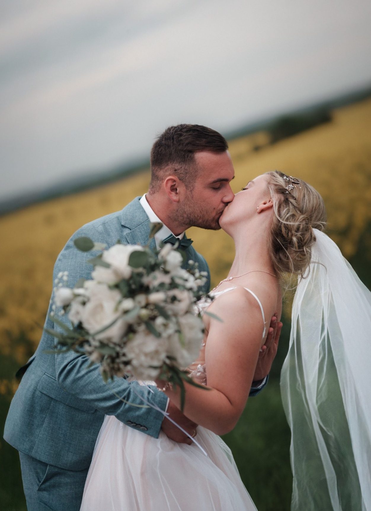 Brautpaar, das sich umarmt, mit einem Blumenstrauß und liebevollem Blick zueinander.