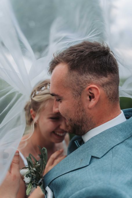 Braut und Bräutigam umarmen sich unter einem transparenten Schleier.