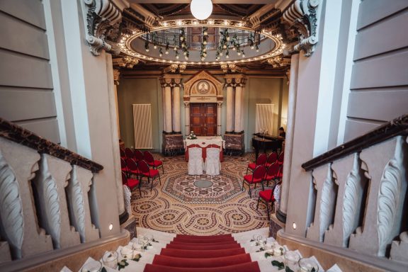 Elegante Treppe mit Blick auf einen festlich dekorierten Saal mit Stuhlreihen und Kronleuchter.