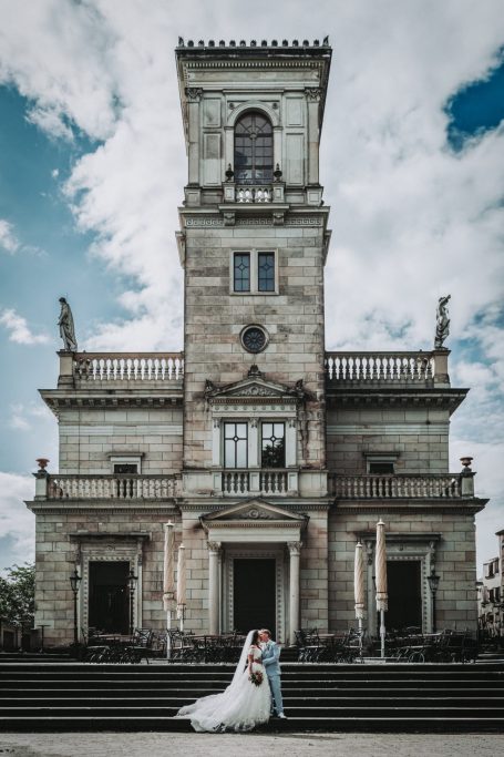Brautpaar umarmt sich vor einem historischen Gebäude an einem sonnigen Tag.