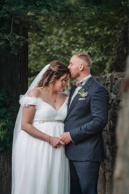 Hochzeitspaar umarmt sich liebevoll vor einer natürlichen Kulisse.