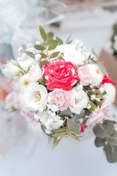 Brautstrauß mit roten und rosa Rosen sowie weißen Blumen und grünen Blättern.