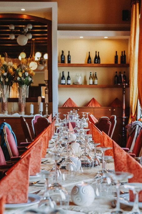 Elegantly gedeckte Tische mit roten Servietten und floraler Dekoration in einem Restaurant.