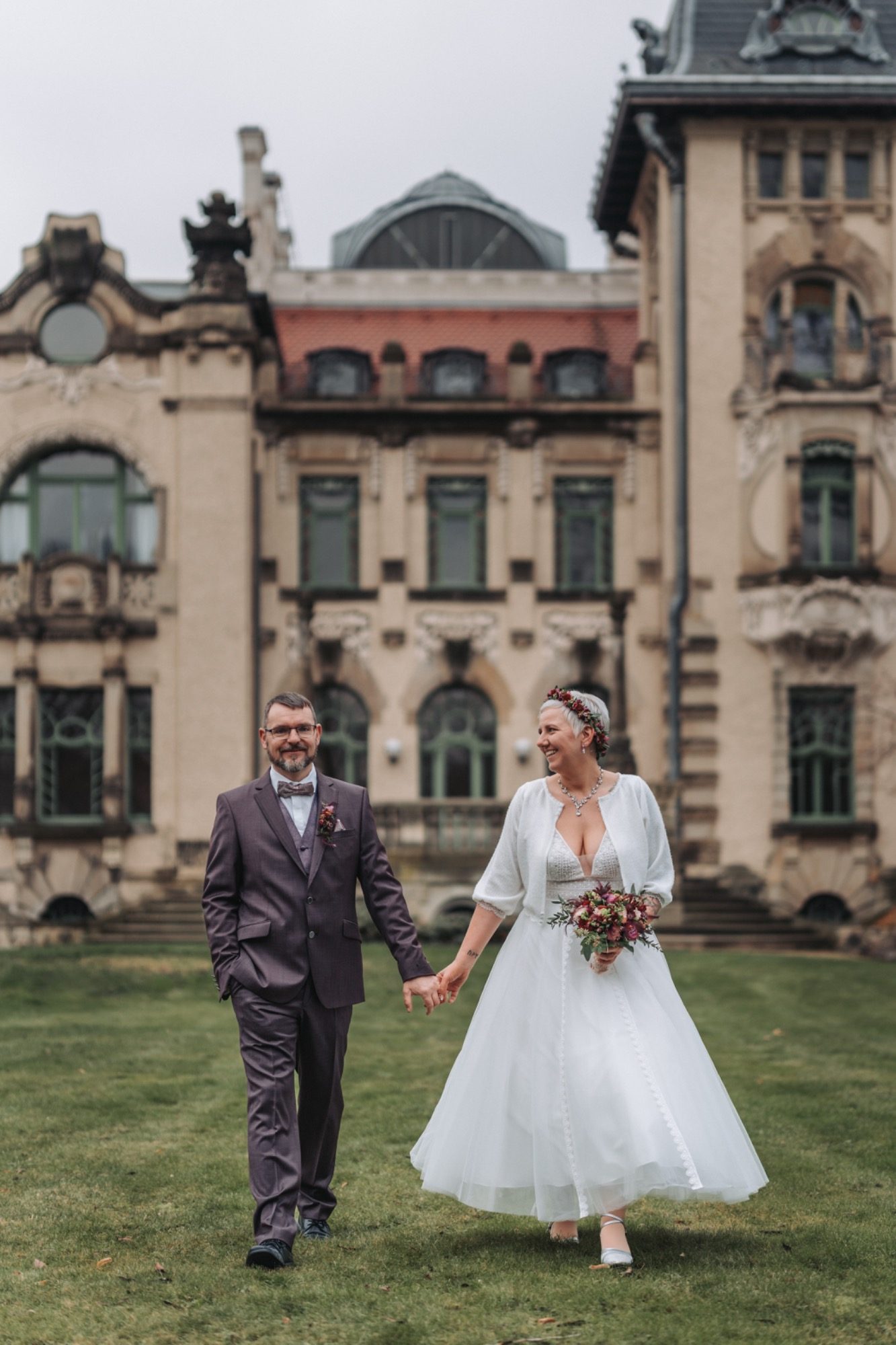 Braut mit offenem Rücken und Spitzenärmel, Brautpaar umarmt sich von hinten.