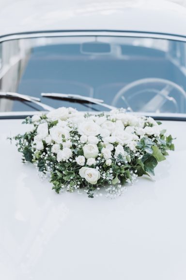 Blumenarrangement aus weißen Blüten auf einer weißen Autokarosserie.