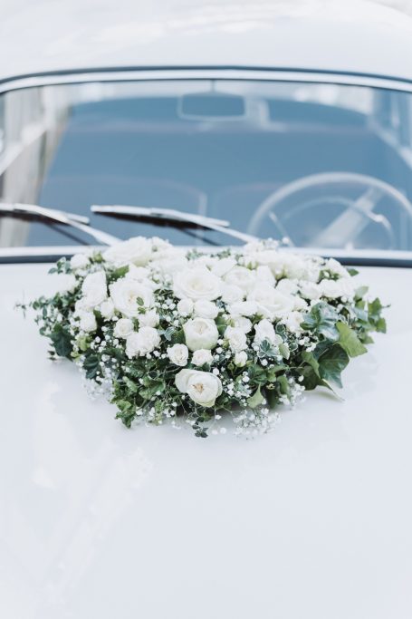 Blumenarrangement aus weißen Rosen und Grün auf der Motorhaube eines Autos.