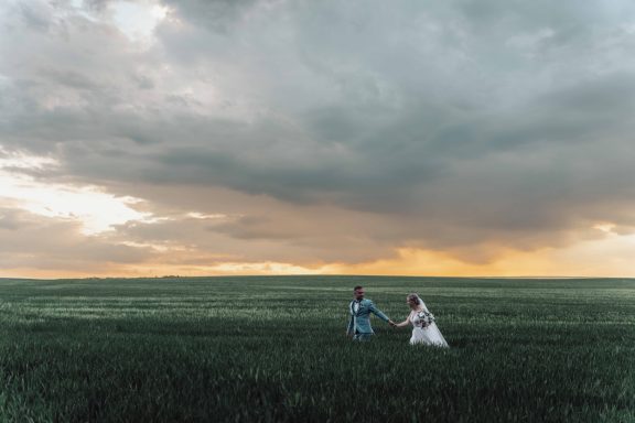 Paar, das Hand in Hand in einem weiten, grasbewachsenen Feld bei Sonnenuntergang läuft.