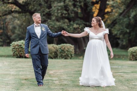 Ein Brautpaar im Freien, Hand in Hand, in eleganter Hochzeitskleidung.