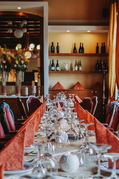 Elegantly gedeckter Tisch in einem Restaurant mit roten Servietten und Blumenarrangements.