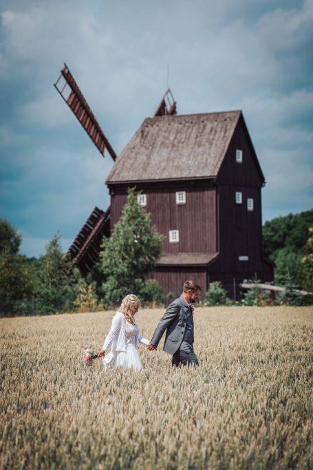 Ein Paar spaziert hand in hand durch ein Feld, hinter ihnen steht eine alte Windmühle.